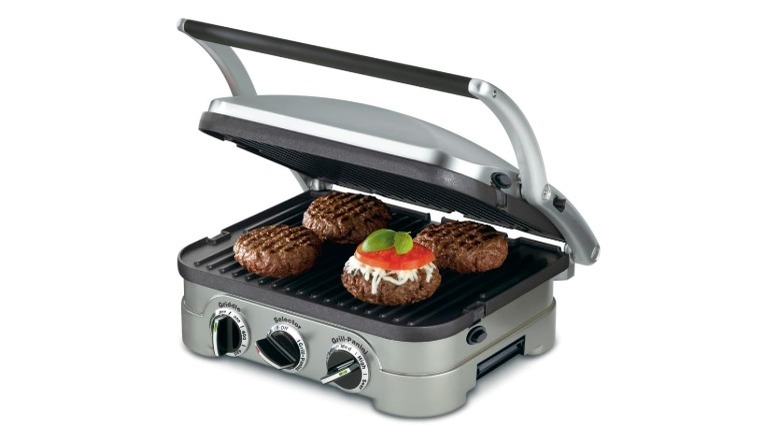 A Cuisinart Griddler and Panini Press with three hamburgers and a cheeseburger topped with a slice of tomato on the grill plate