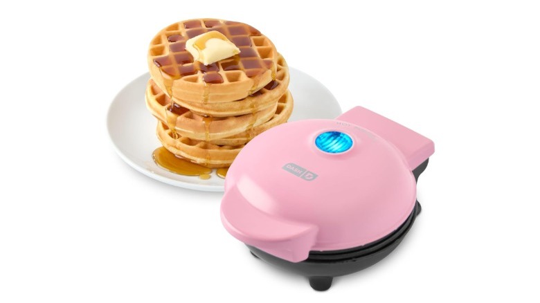 A Dash Mini Waffle Maker and a stack of waffles with a pat of butter on top and syrup dripping down the sides