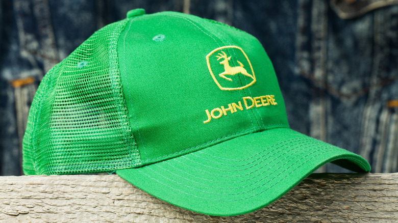 Green John Deere baseball cap on wooden fence.