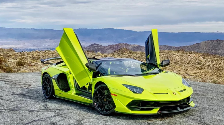 A green 2021 Lamborghini Aventador SVJ Roadsterwith its doors open and desert in the background