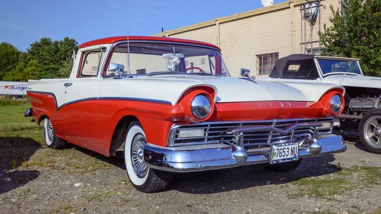 A red and white Ford Ranchero parked on gravel