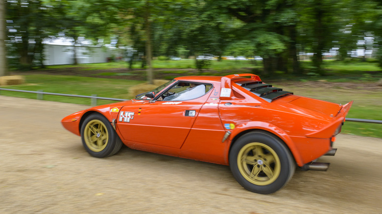 Red Lancia Stratos HF Stradale driving on gravel rally course