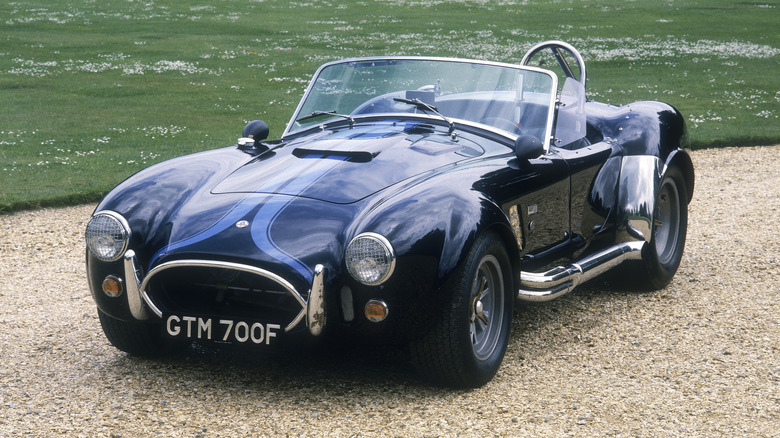 Blue Shelby Cobra parked on gravel in front of grass