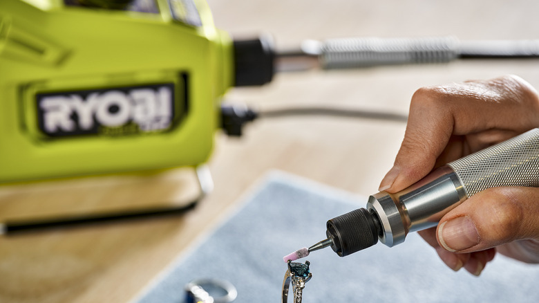 Hand holding a rotary precision tool polishing a gemstone in a ring