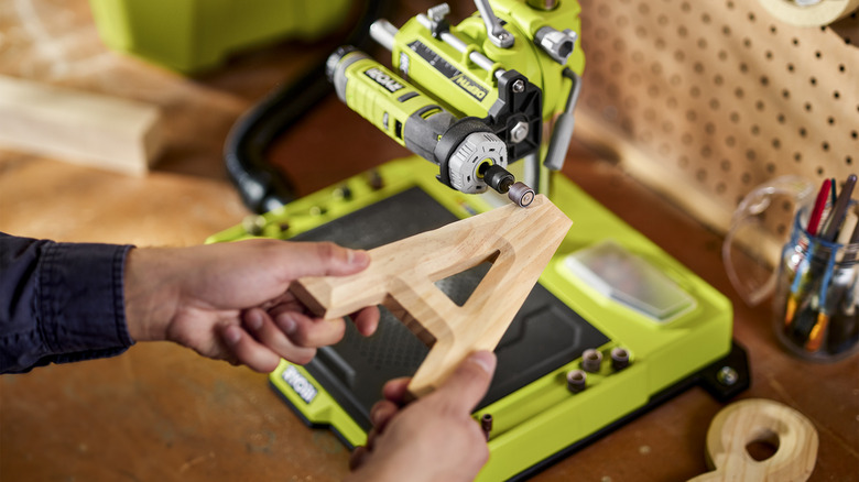 Hands holding a wooden letter A using a rotary sander