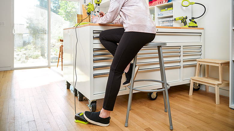 Bottom half of a person on a stool with one foot on a pedal in a craft room