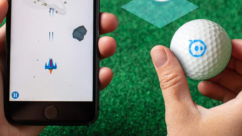 A person holding a Sphero golf ball and a smartphone