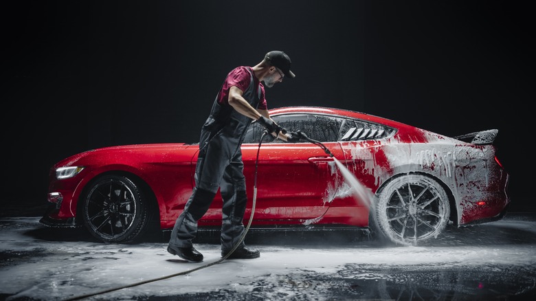 A man washing a red sports car with a powerwasher