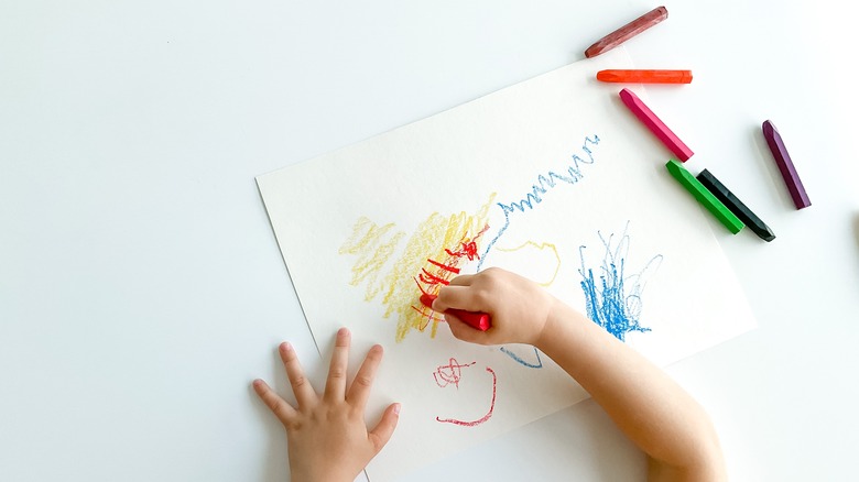 A child coloring with Crayons on paper