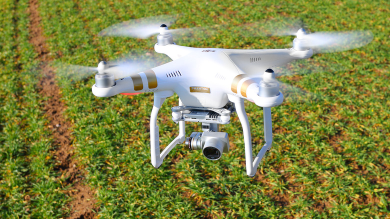 A shot of a DJI Phantom quadcopter drone in flight over a green field.