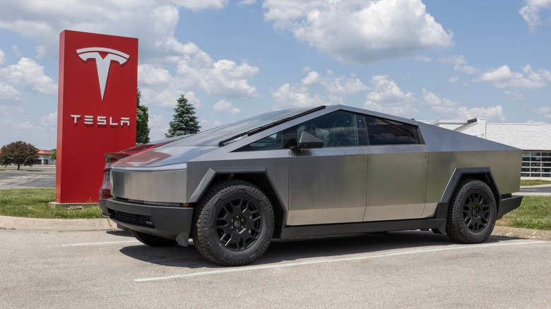 A Tesla Cybertruck sitting next to a Tesla sign