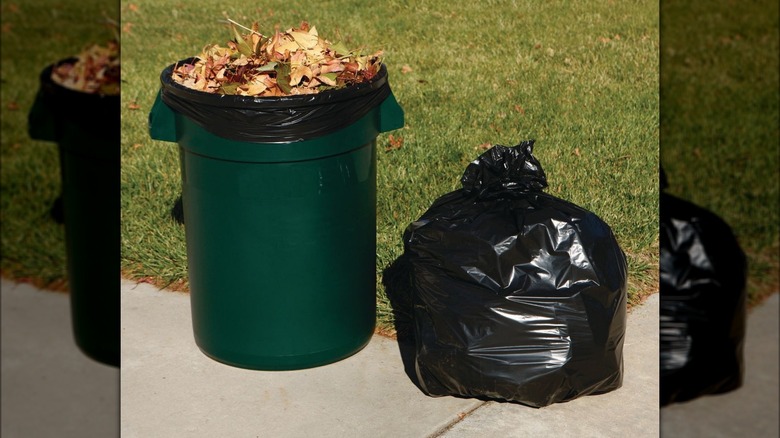 Green trash can with a black trash bag inside filled with leaves