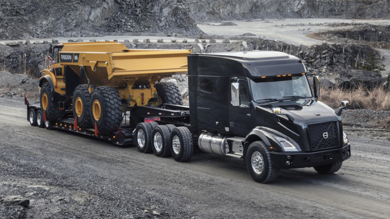 A Volvo VNX 740 hauling a dump truck on a dirt path