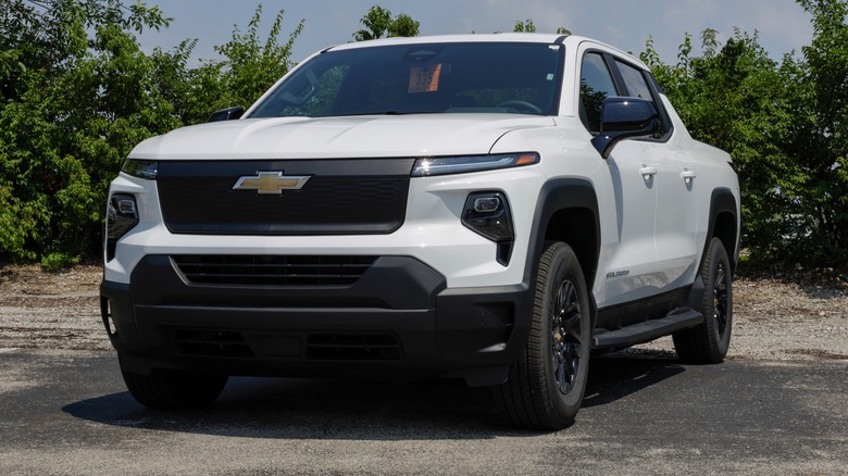 A white Chevy Silverado EV parked near bushes