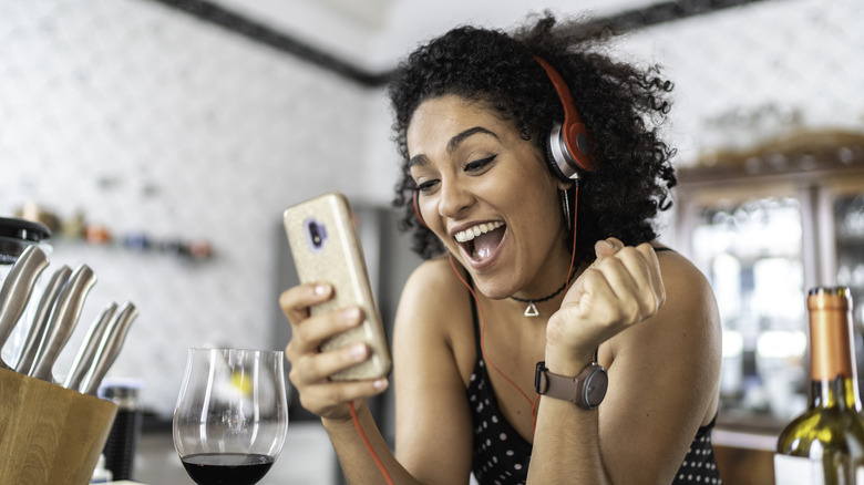 woman wearing headphones, using her phone, and smiling