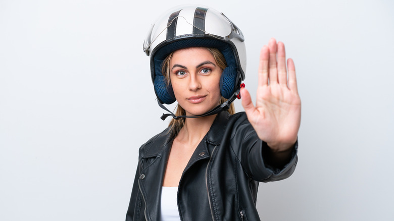 Person wearing a motorcycle helmet holding their hand out in a "stop" gesture.