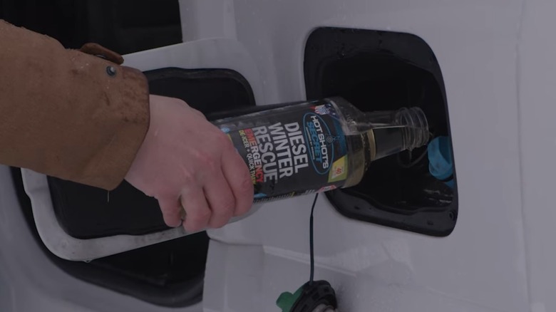 A person pouring a de-gelling additive into their fuel tank