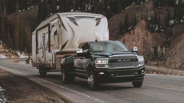 A ram 3500 pickup truck pulling a large trailer up what appears to be a slight incline with snow in the background