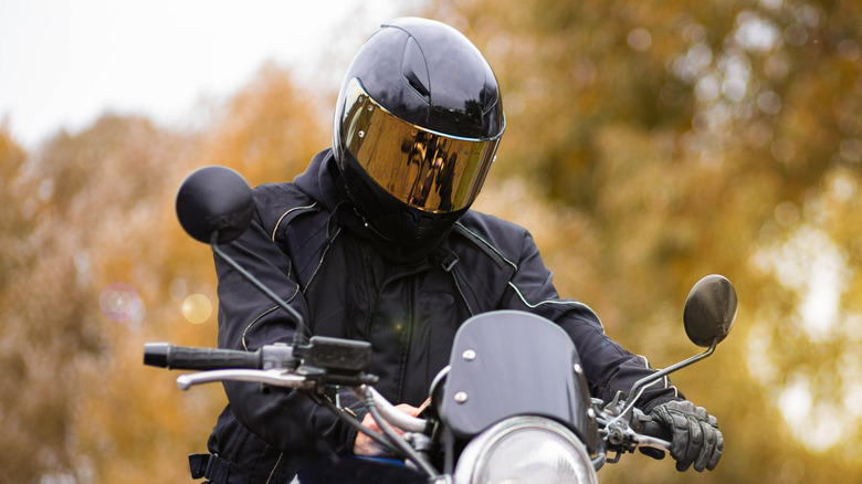 A motorcycle rider sitting outside on their bike and wearing a helmet