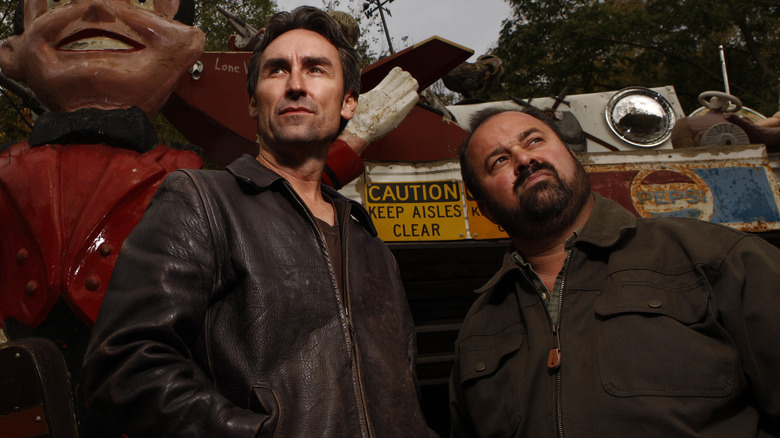 Mike Wolfe and Frank Fritz posing in junkyard among antiques