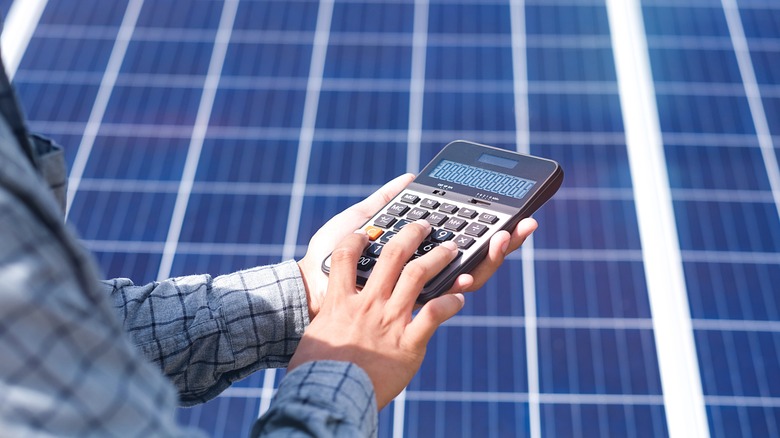 man using calculator near solar panels