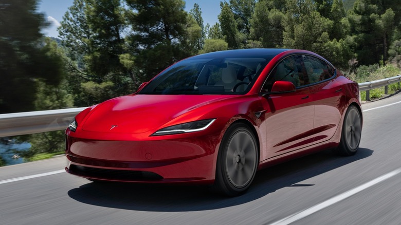 a red Tesla Model 3 driving on a road