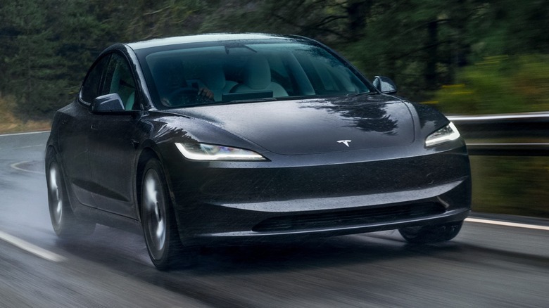 a black Tesla Model 3 driving in the rain