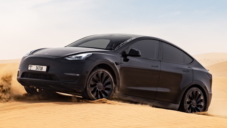 a black Tesla Model Y driving on sand