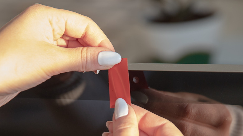 hands placing a small piece of red tape over a built-in webcam on a computer monitor