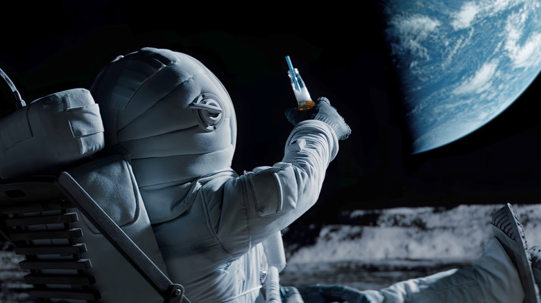 An astronaut lounging on the moon greets Earth by holding up a bottle with a straw inside