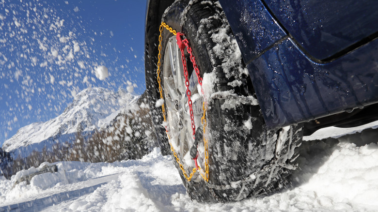 A blue car using snow chains drives through snow.