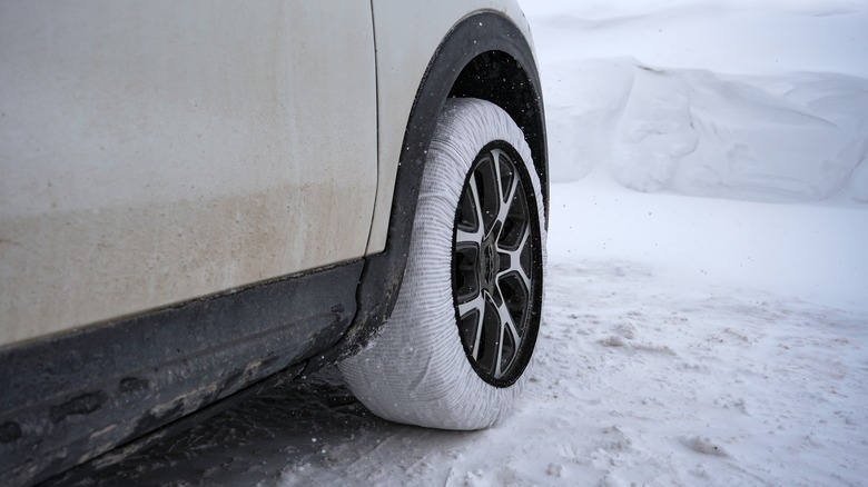 A tan car wearing a snow sock on a tire.