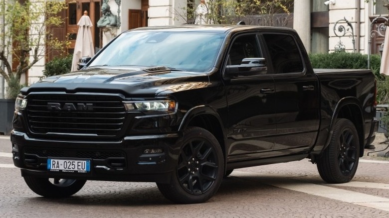 A black 2025 Ram 1500 Laramie parked on a paved surface in front of a building.