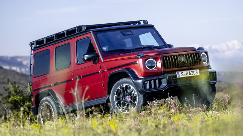 Front 3/4 view of red Mercedes-AMG G 63 climbing a grassy hill