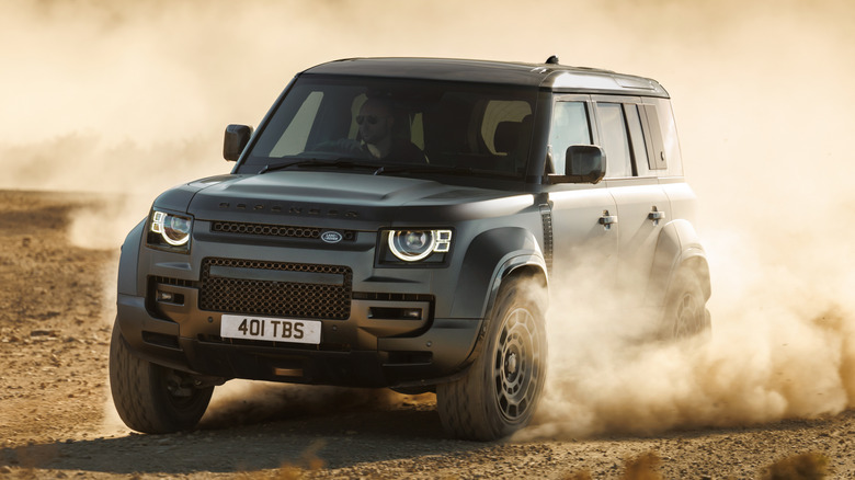 Front 3/4 view of gray Land Rover Defender driving on dirt