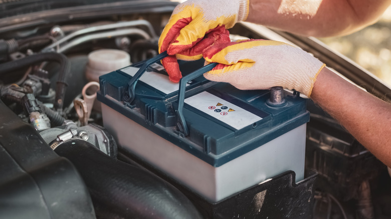 A person wearing gloves lifting a car battery.