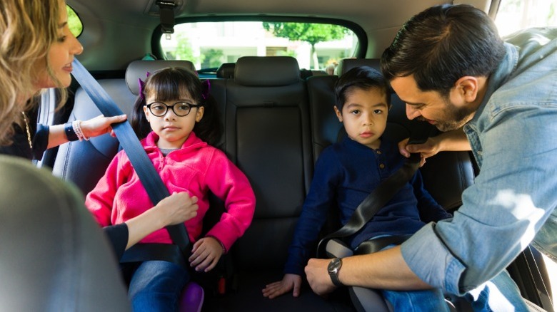 Parents securing their kids on booster seats in a car