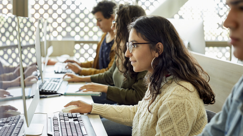 Girl with eyeglasses using a desktop computer next to other students