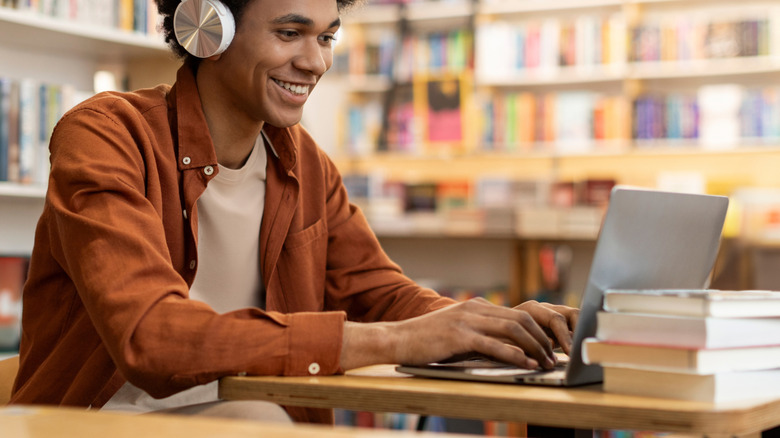 A student wearing headphones in a library and using a laptop