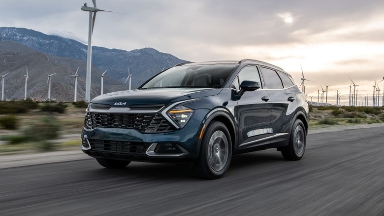 2025 Kia Sportage Hybrid driving on a road with mountains and wind turbines  in the background