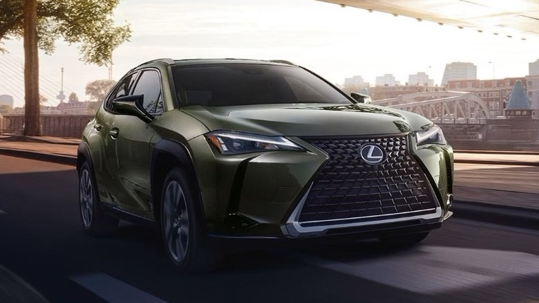 Nori Green Pearl 2025 Lexus UX driving on a road with trees and buildings in the background