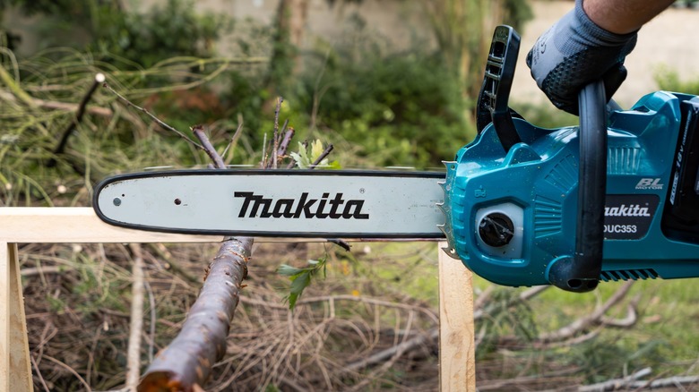 Makita top-handle chainsaw cutting through branch.