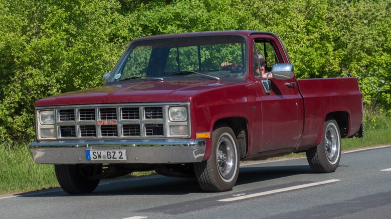 A red 1978 GMC square body driving on the road