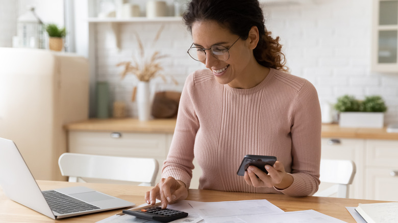 A woman checks her phone and uses a calculator