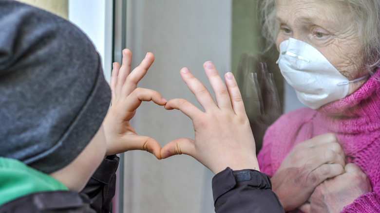 child making heart through glass to old lady