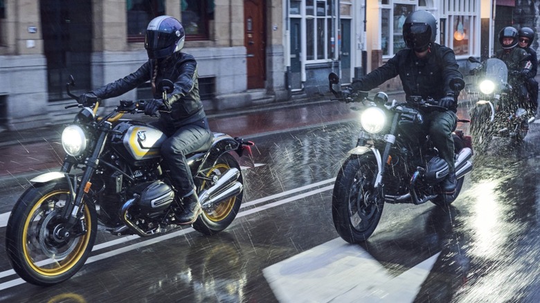 A trio of Cafe Racer motorcycles riding on a wet city street.