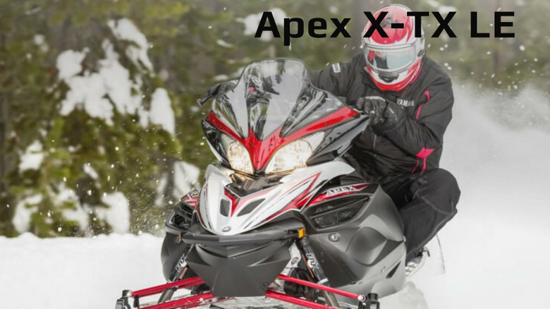 Front view of black and red Apex snowmobile driving across snow.