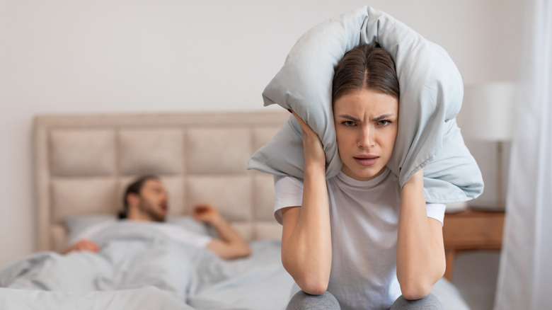 A woman is using a pillow to block her partner's snoring