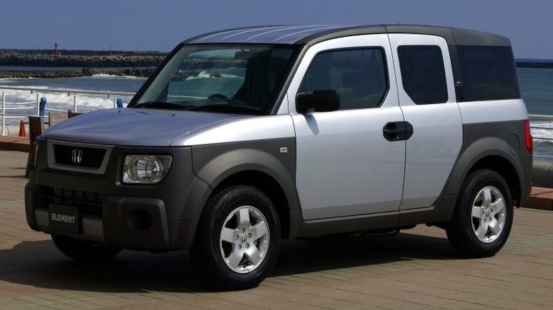 Satin Silver Metallic Honda Element parked on a pavement near a body of water