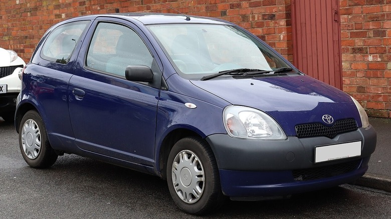 Blue Toyota Yaris parked on street in front of red brick building